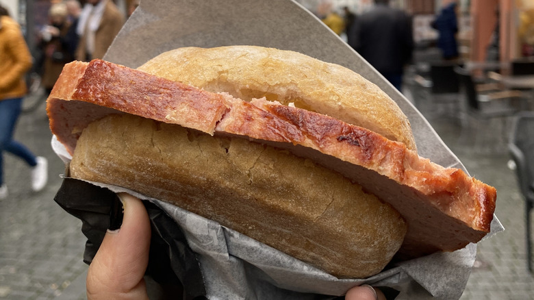 A leberkase sandwich on a hard roll, wrapped in a paper napkin