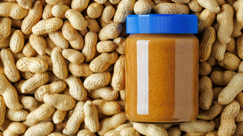 An unopened jar of peanut butter sitting on top of a pile of peanuts.