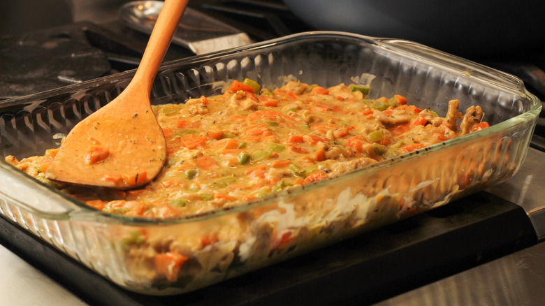 Glass baking dish with layer of creamy chicken casserole and wooden spoon