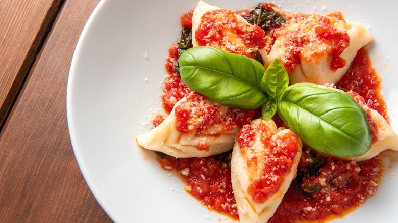 A bowl of culurgiones with tomato sauce and fresh basil leaves