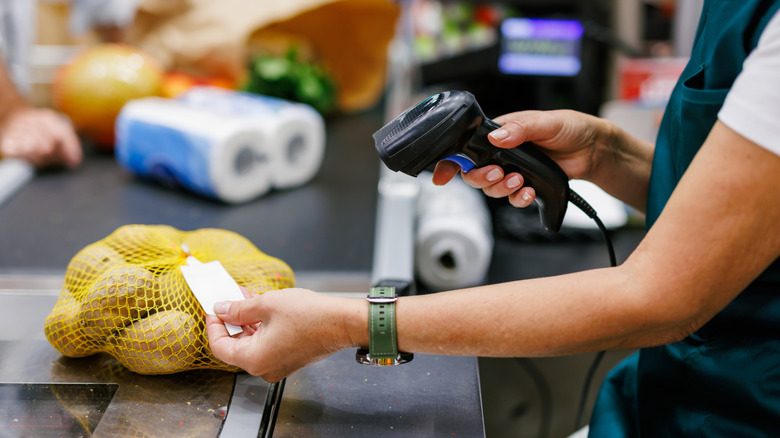 A person scanning a barcode on a bag of potatoes in the checkout lane of a grocery store