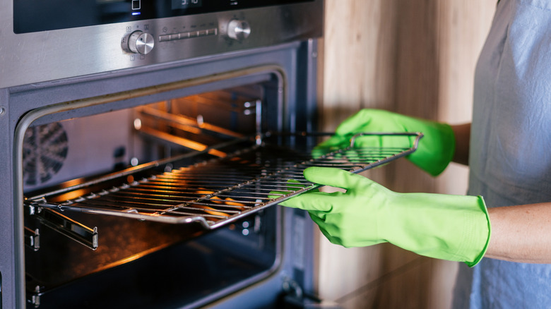 Person wearing green gloves pulls out dirty oven rack