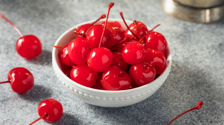 Bright red maraschino cherries with stems in a small white bowl