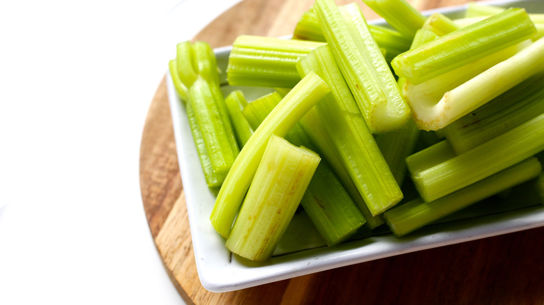 A white, square plate of cut, raw celery stalks on a wooden serving board