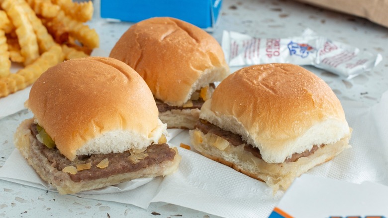 white castle sliders on paper napkins next to a pile of crinkle fries and several ketchup packets