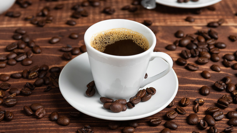 White cup of coffee on a saucer, surrounded by loose coffee beans