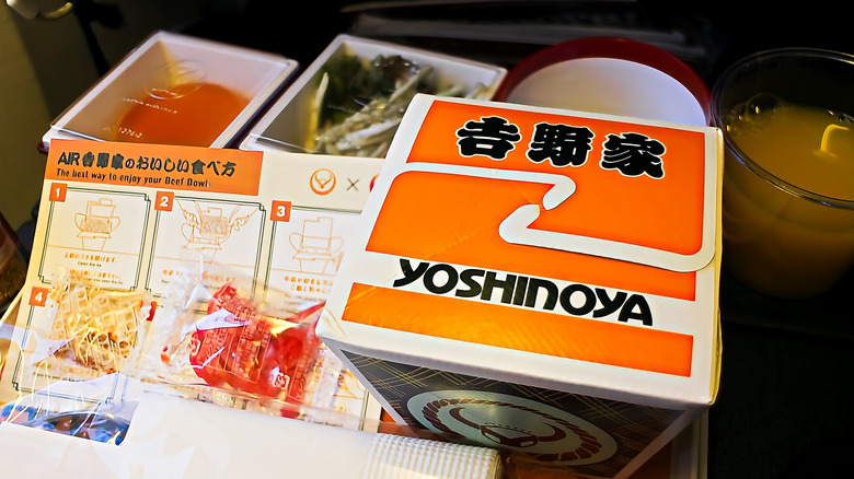 A meal with sides from Yoshinoya still in its packaging alongside a menu on a tray