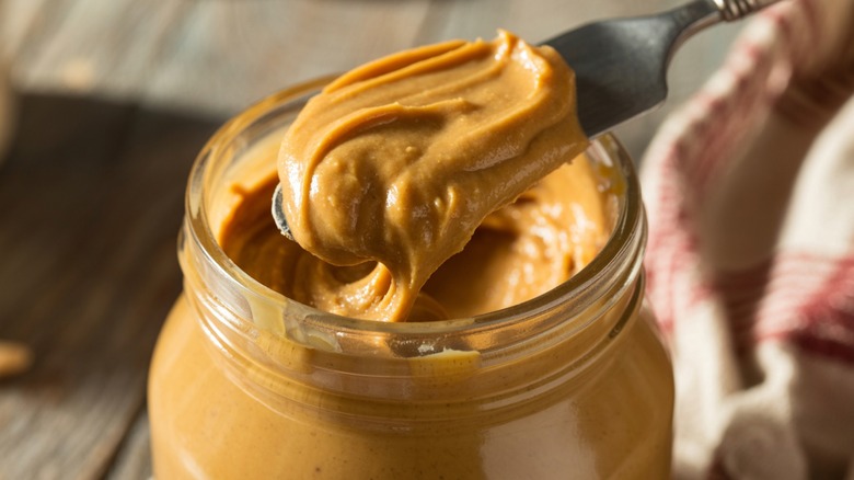 Scooping peanut butter from a jar using a knife