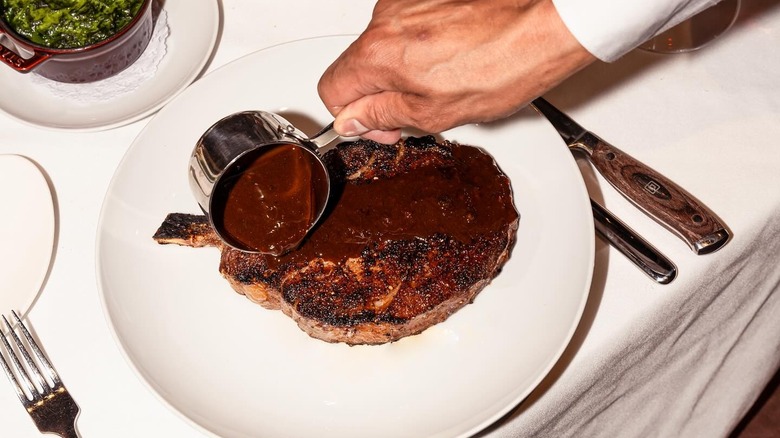 server pouring sauce on steak at Delmonico's table