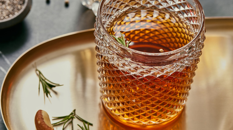 A cut glass tumbler full of whiskey, garnished with fresh rosemary