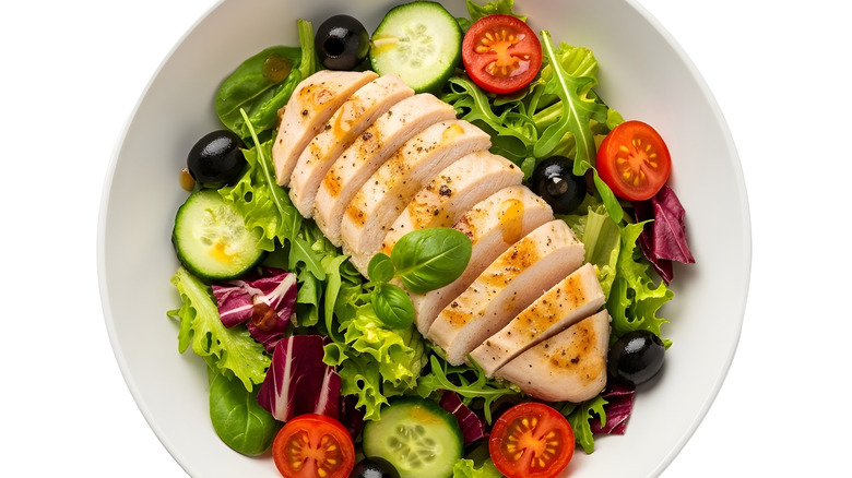 Grilled chicken on mixed green salad with tomatoes and olives.