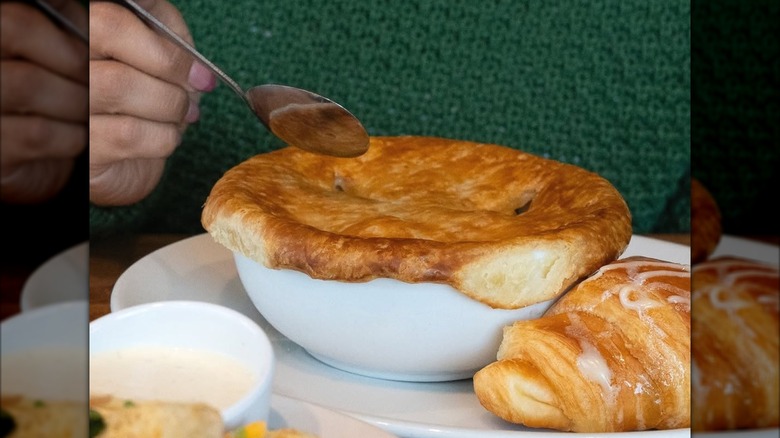 A person in a green sweater about to eat Cheddar's Scratch Kitchen chicken pot pie with a honey butter croissant.