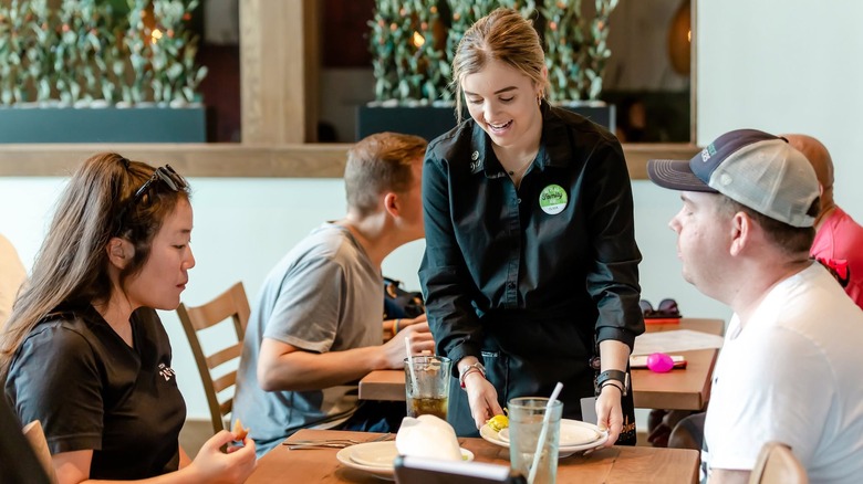 An Olive Garden waitress picking up plates from two diners in the restaurant.