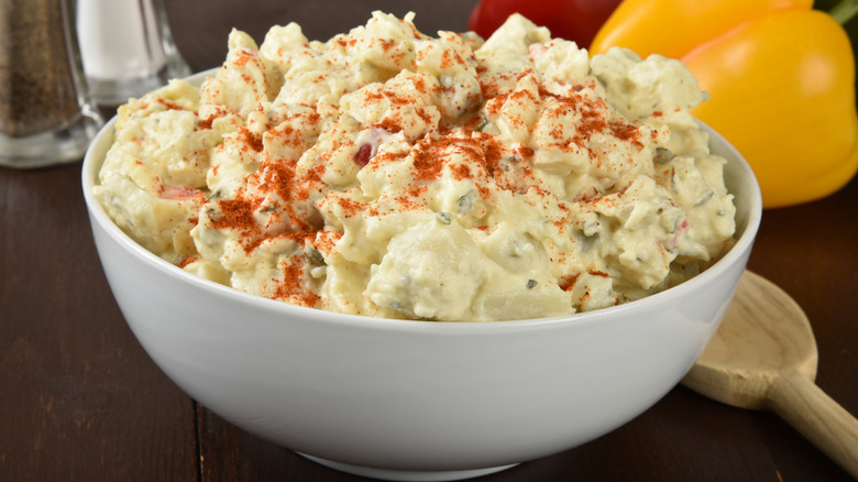 A bowl of seasoned potato salad with peppers in the background