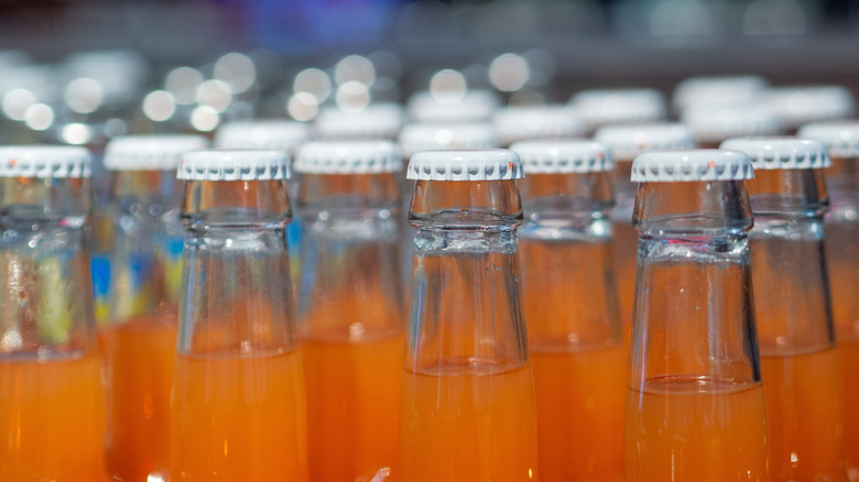 Glass bottles filled with orange soda sealed with white metal caps