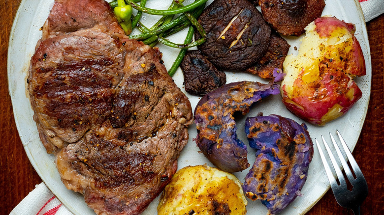 A delmonico steak served with potatoes, mushrooms, and green beans on a earthenware plate