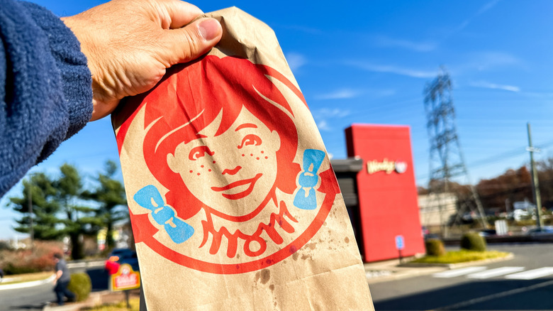 A Wendy's bag being held up in front of a Wendy's restaurant