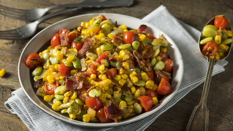 a bowl of succotash with napkin and cutlery