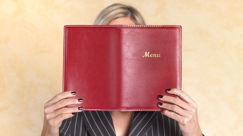 A woman holding a restaurant menu over her face.