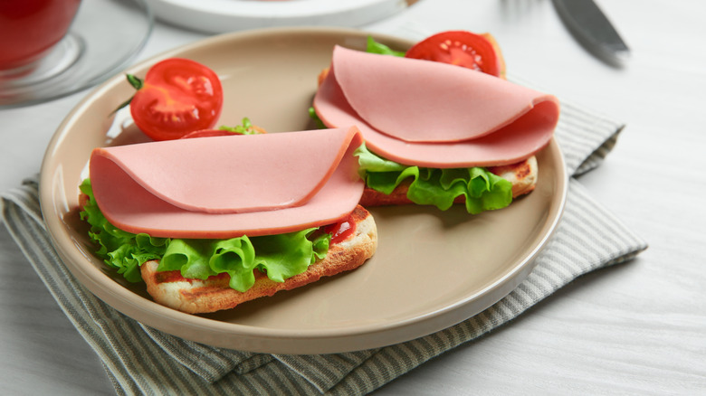 Folded slices of bologna on top of two pieces of bread and lettuce.