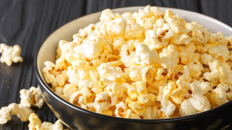 A bowl of white-yellow cheddar popcorn against a wooden surface