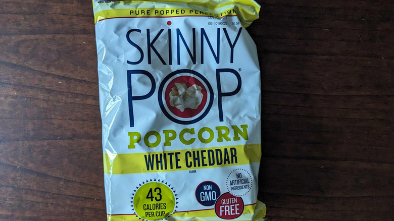 A bag of SkinnyPop cheddar popcorn against a wooden surface