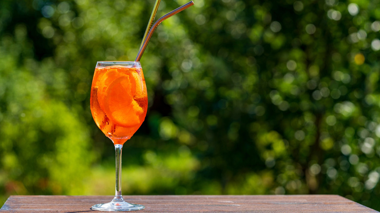 A glass of a spritz cocktail with two straws on it outside during the day.