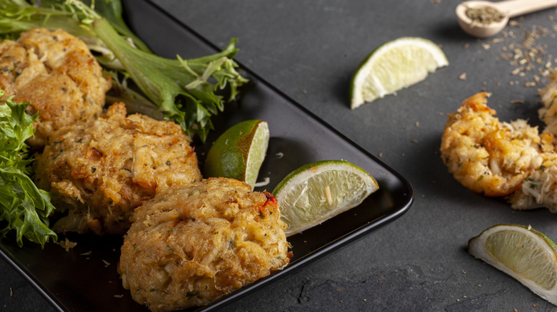 Browned crab cakes served on a black plate with lime wedges