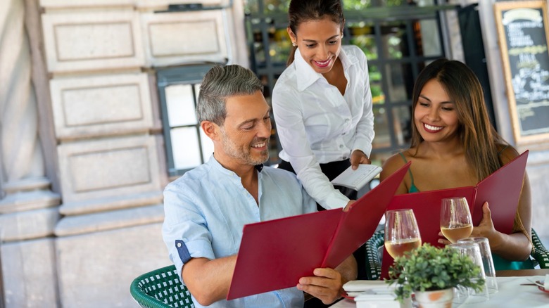 Server recommending menu item to couple at outside dining restaurant