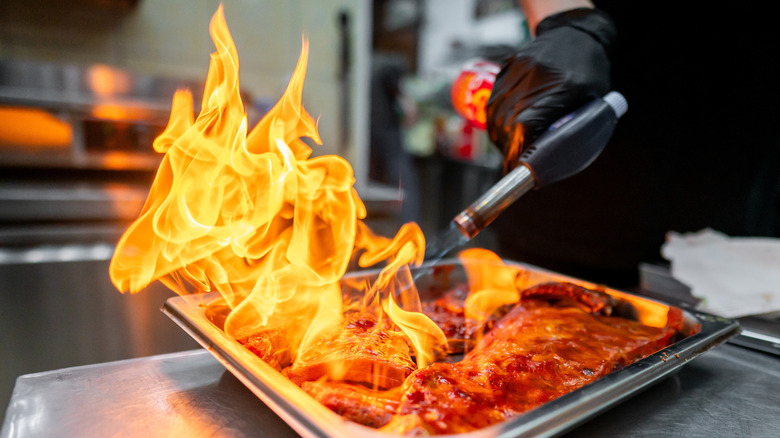 A chef uses a kitchen torch to caramelize food in a pan