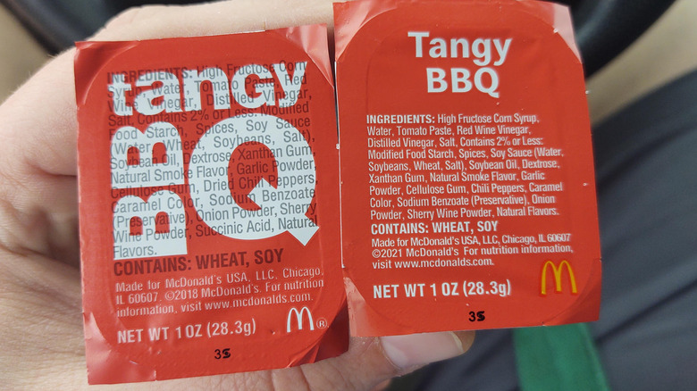 A hand holding two small cups of McDonald's Tangy BBQ Sauce