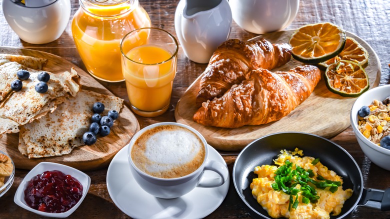 A rustic feast for breakfast that includes eggs, bread, museli, a cappuccino, and some pastries.
