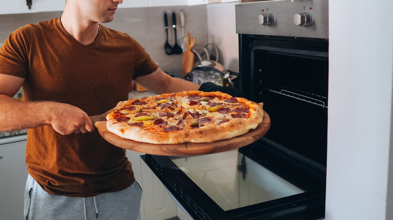 A man putting a pizza into an oven using a pizza paddle