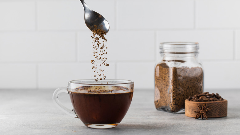 Spoon sprinkling instant coffee into glass mug