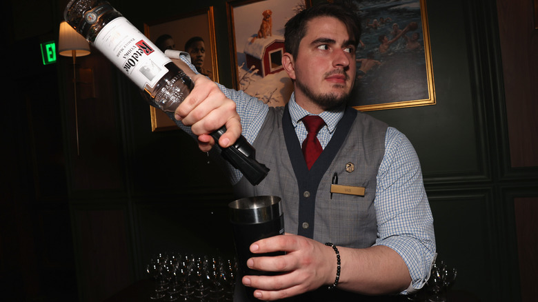 A bartender looks to the side while pouring from a bottle of Ketel One into a shaker
