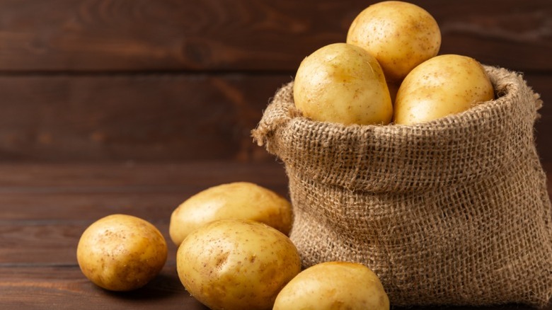 A number of potatoes in and near a burlap sack.