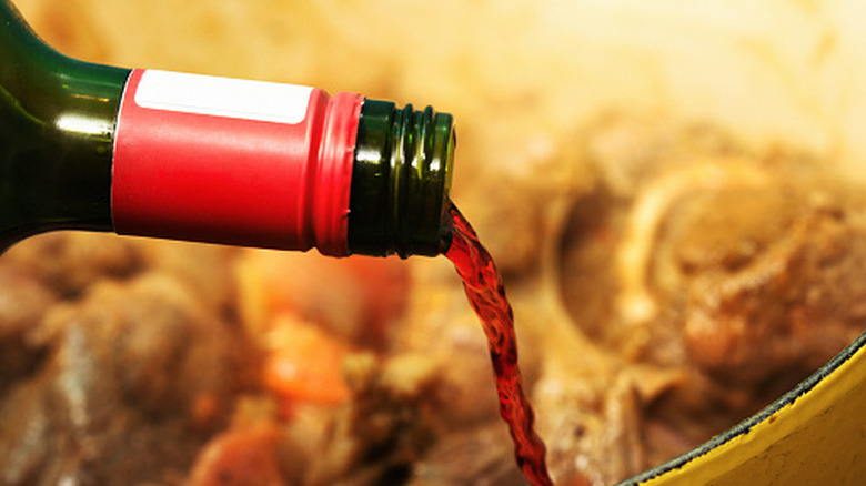 Bottle of wine being poured into a pot containing meat