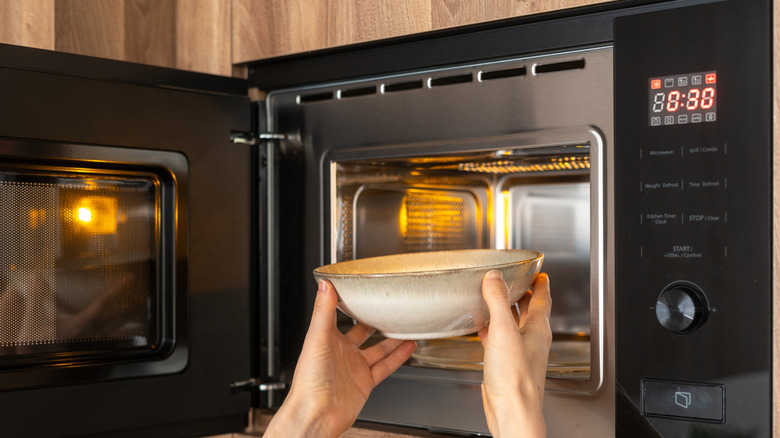 Two hands grabbing a bowl from a microwave