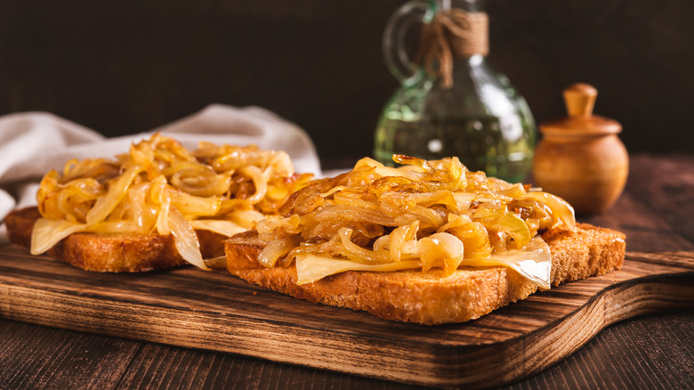 Caramelized onions on top of toasted bread on a wooden cutting board, near a bottle of oil