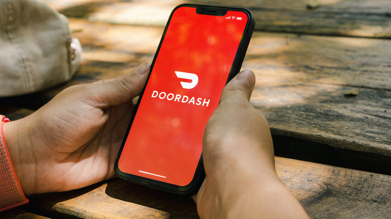 Two hands holding a phone opening the DoorDash app