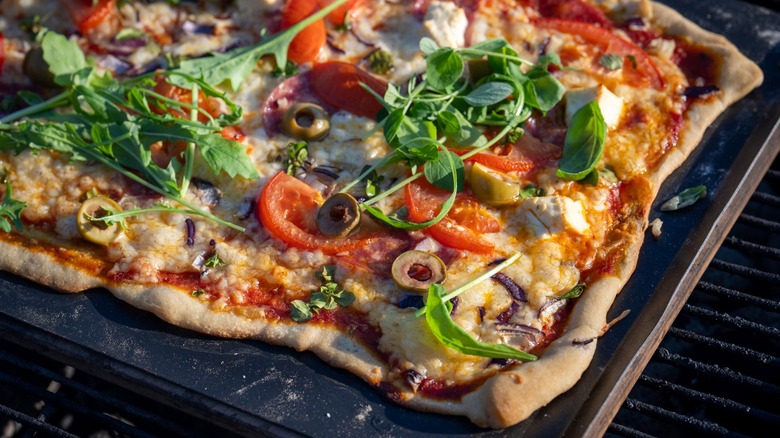Pizza with olives, tomatoes, and greens on grill