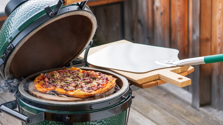 Pizza on grill with pizza peel nearby