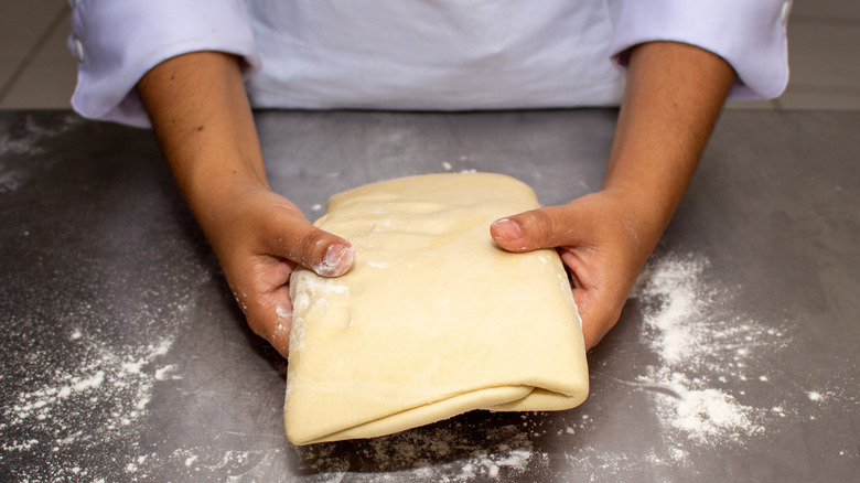 cook holds folded puff pastry in hands before parking