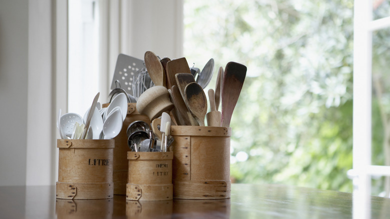 Assortment of kitchen utensils and tools in wooden containers with greenery in background
