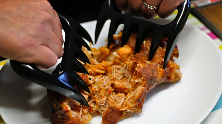 two hands shredding meat on a plate with meat claws