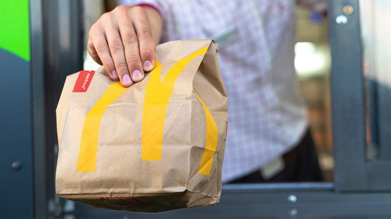 Person handing McDonald's bag to customer in drive-thru