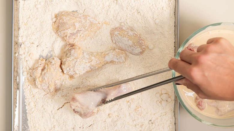 Person dredging chicken for frying with tongs