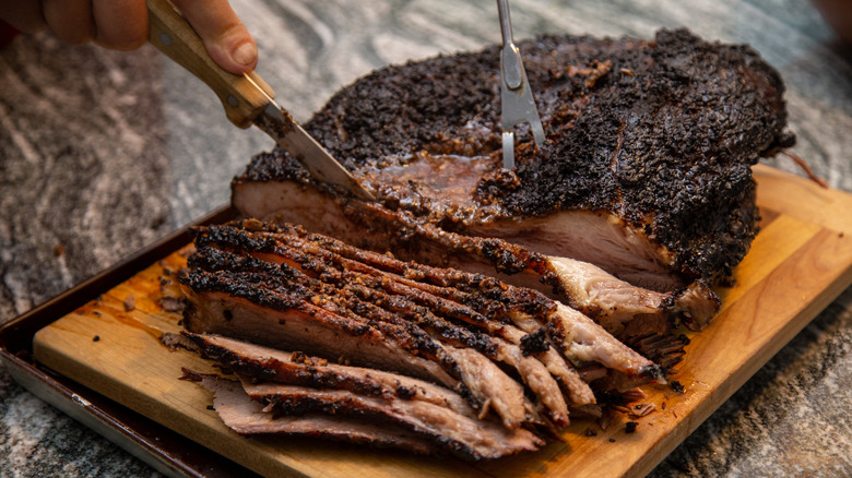 A well-seasoned smoked brisket being sliced into pieces on a wooden board