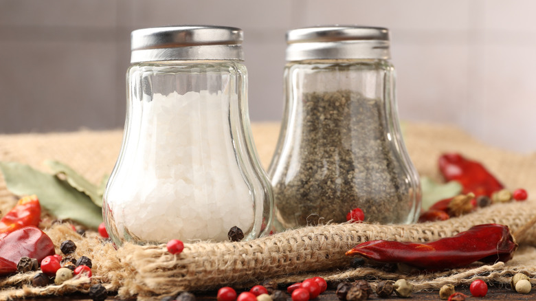 Glass salt and pepper shakers beside peppers and peppercorns