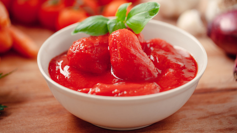 Canned whole peeled tomatoes in a white bowl with a fresh basil garnish